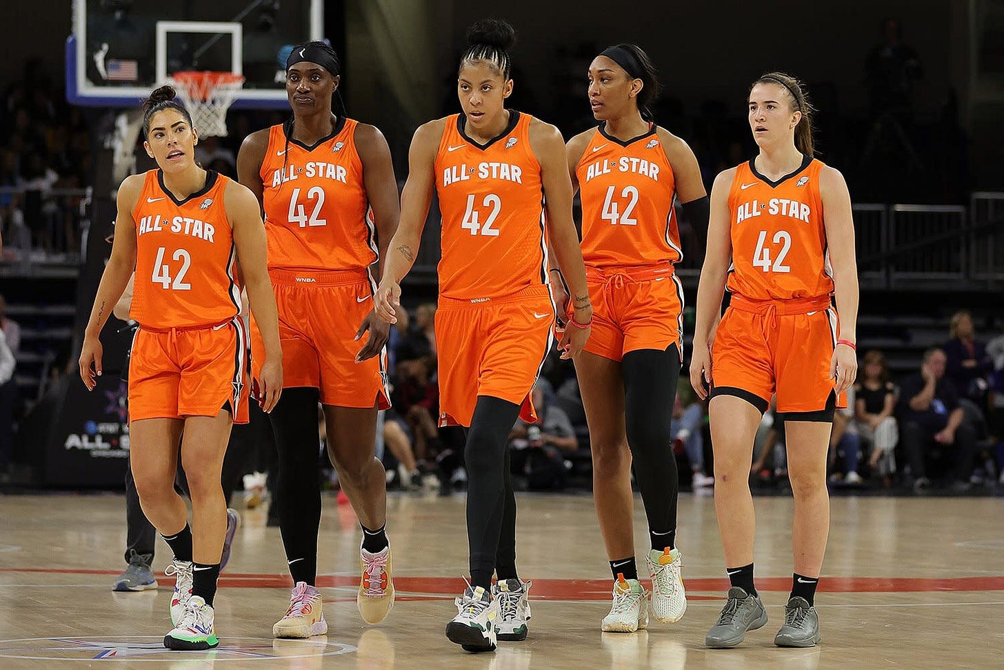 Five players walking on a basketball court in orange jerseys that all say "All-Star 42"