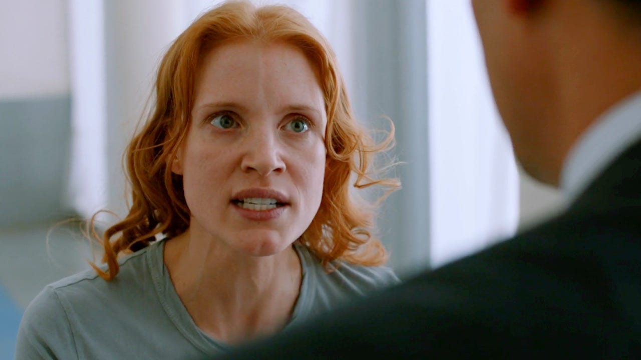 Chastain in a t-shirt looking intense in close up; there's a blurred suit guy in foreground who she is talking to. Chastain in a t-shirt looking intense in close up; there's a blurred suit guy in foreground who she is talking to.