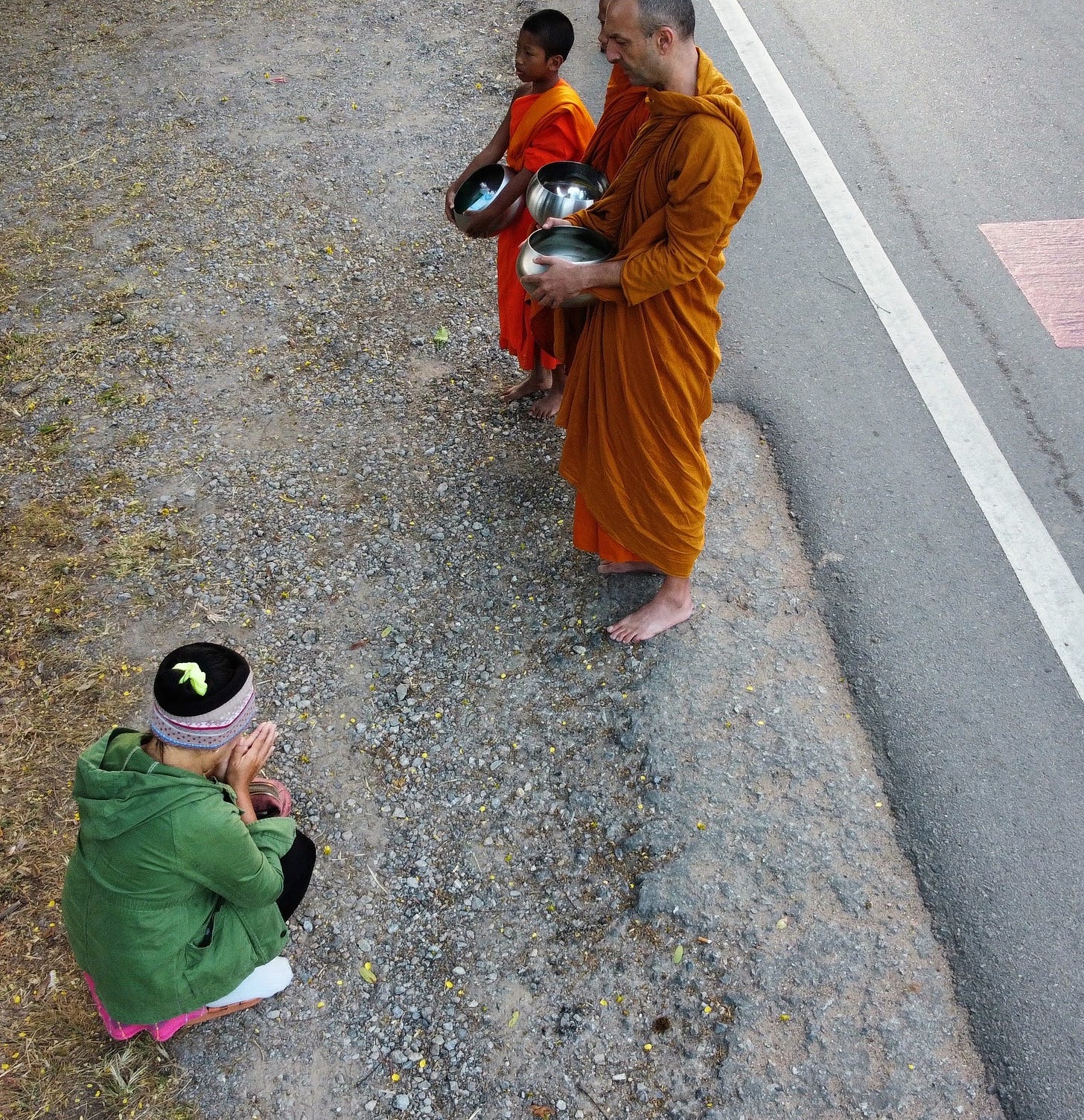 monk and two mink novices on alms round and a thai laday on her knees bowing
