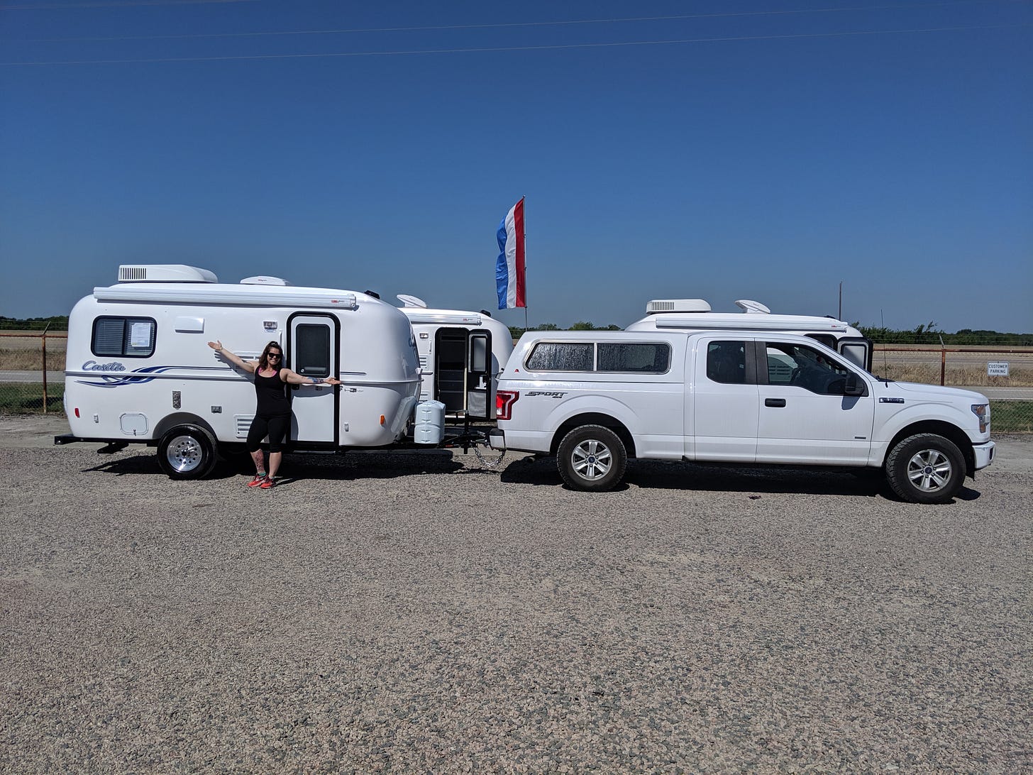 A woman stands in front of a white travel trailer attached to a white truck in the desert