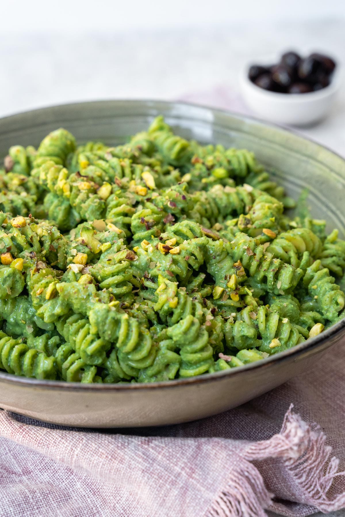 Spinach pasta served with chopped pistachios and black olives.