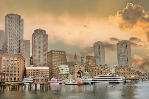 Free Elegant view of Boston Harbor with skyscrapers and boats at sunset, capturing urban charm. Stock Photo