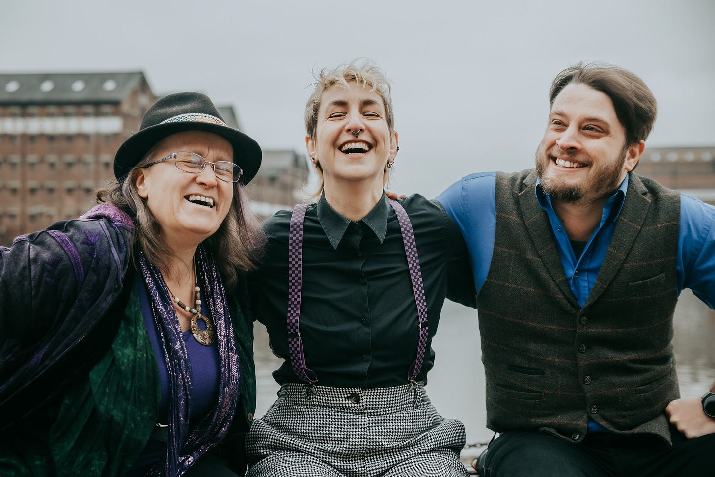 Three musicians sit on a quayside wall, laughing.