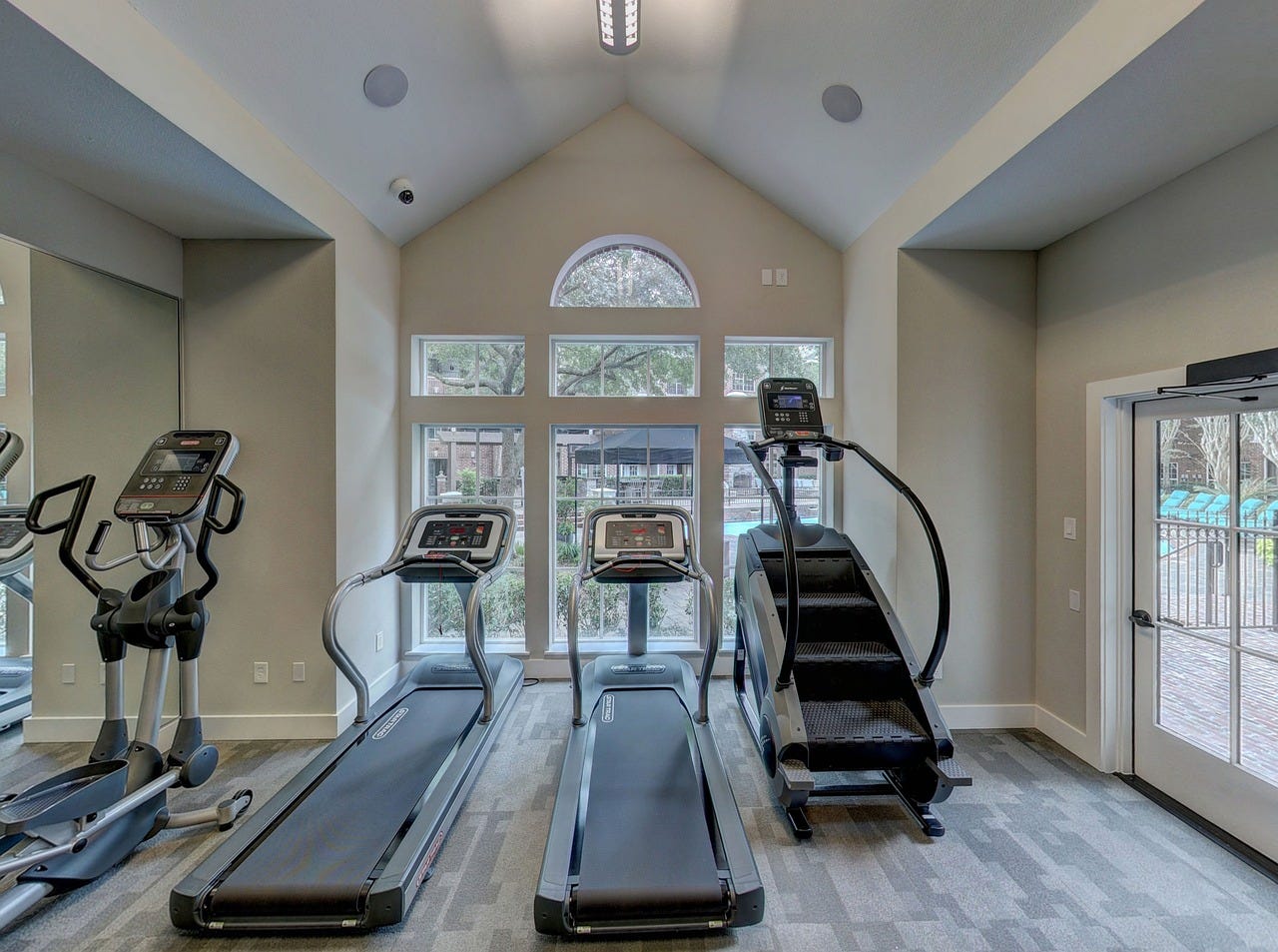 A home gym set up. An elliptical trainer, 2 treadmills and a stair climber sit in a high-ceilinged room.