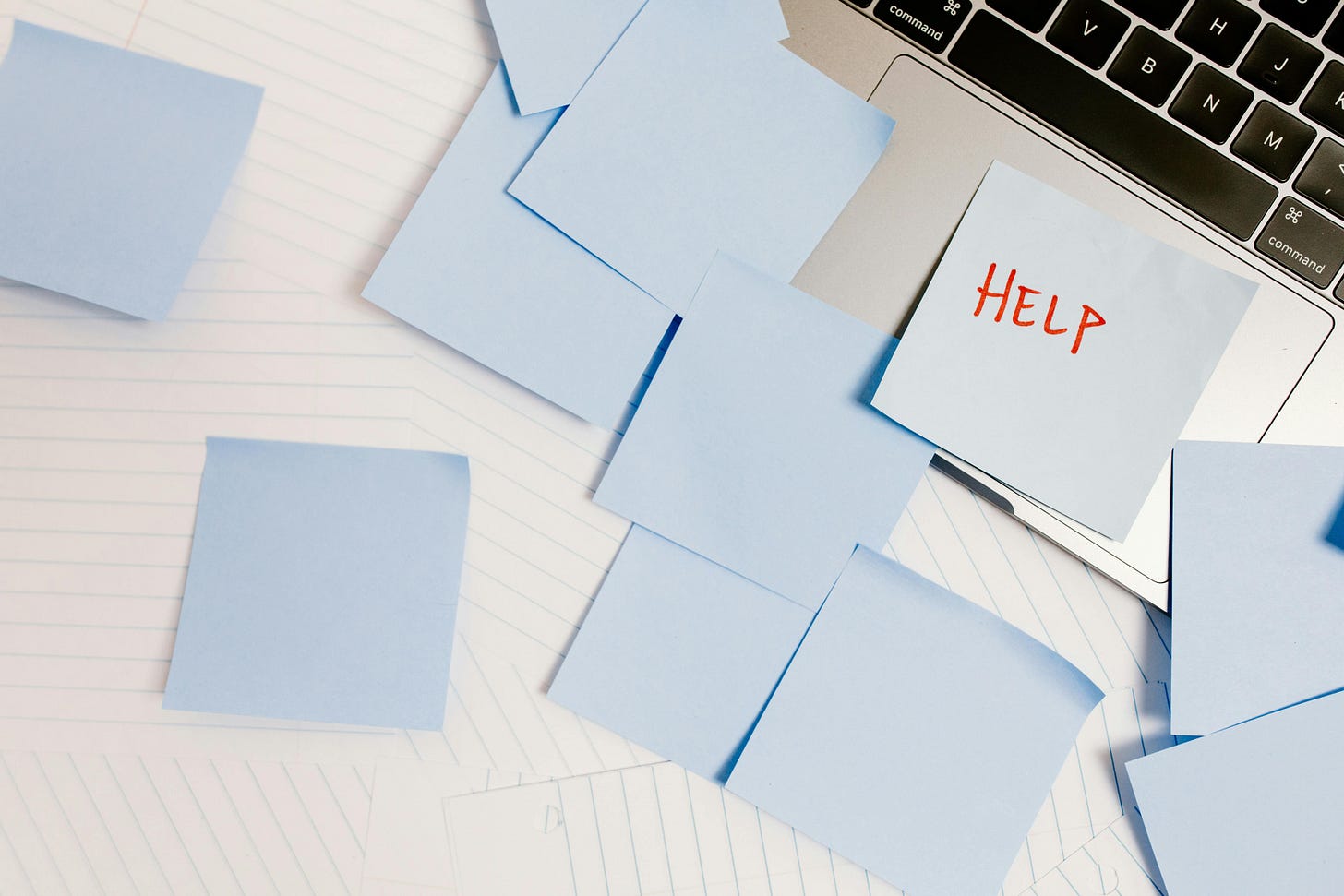 Photo of a bunch of blue sticky notes on and around a laptop. One of them reads "help me"