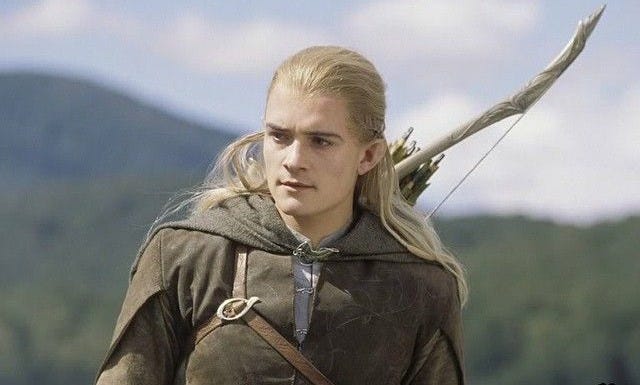 This may contain: a man with long blonde hair wearing a brown outfit and holding an arrow in his hand