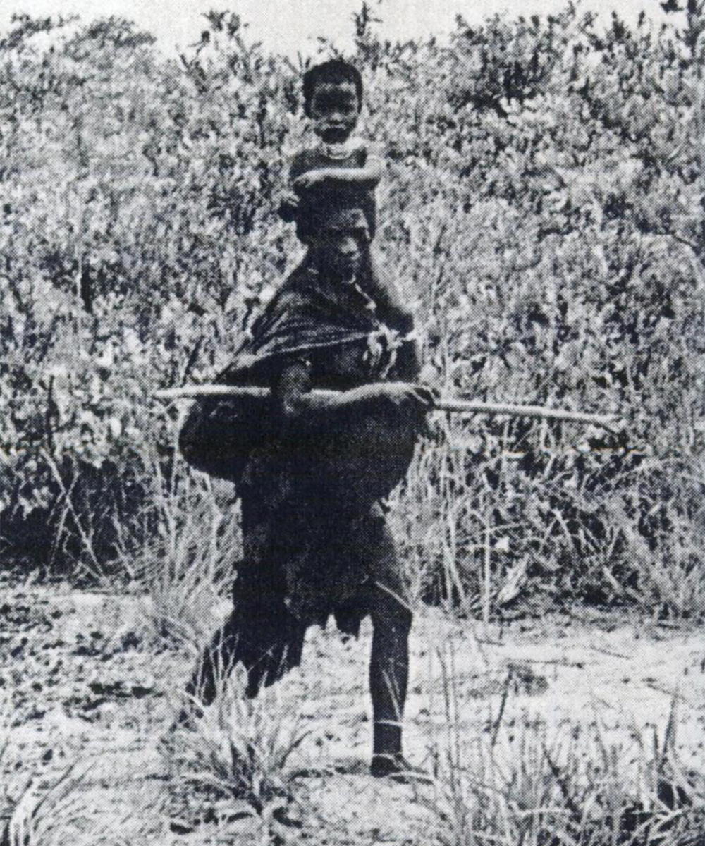 A black and white image of a pregnant woman carrying a spear in one hand and a child in the other