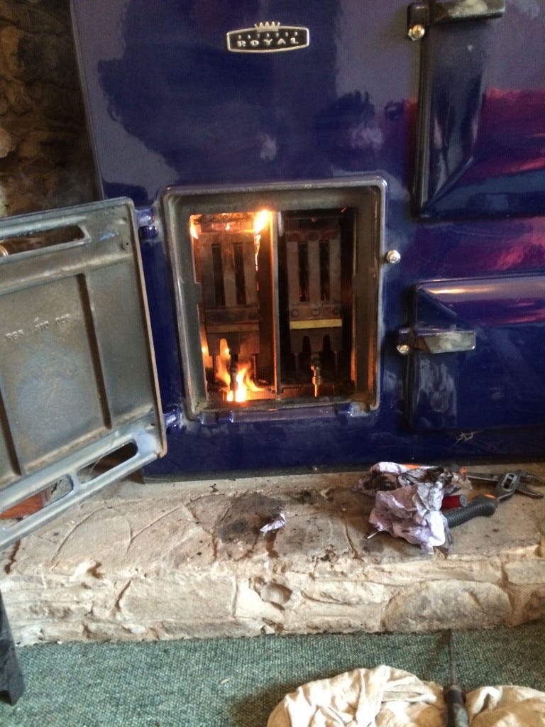 Royal blue Rayburn with the door open, and liquid flame dripping in the lighting box. Oily rags and tools on the stone slab in front. Exciting day!