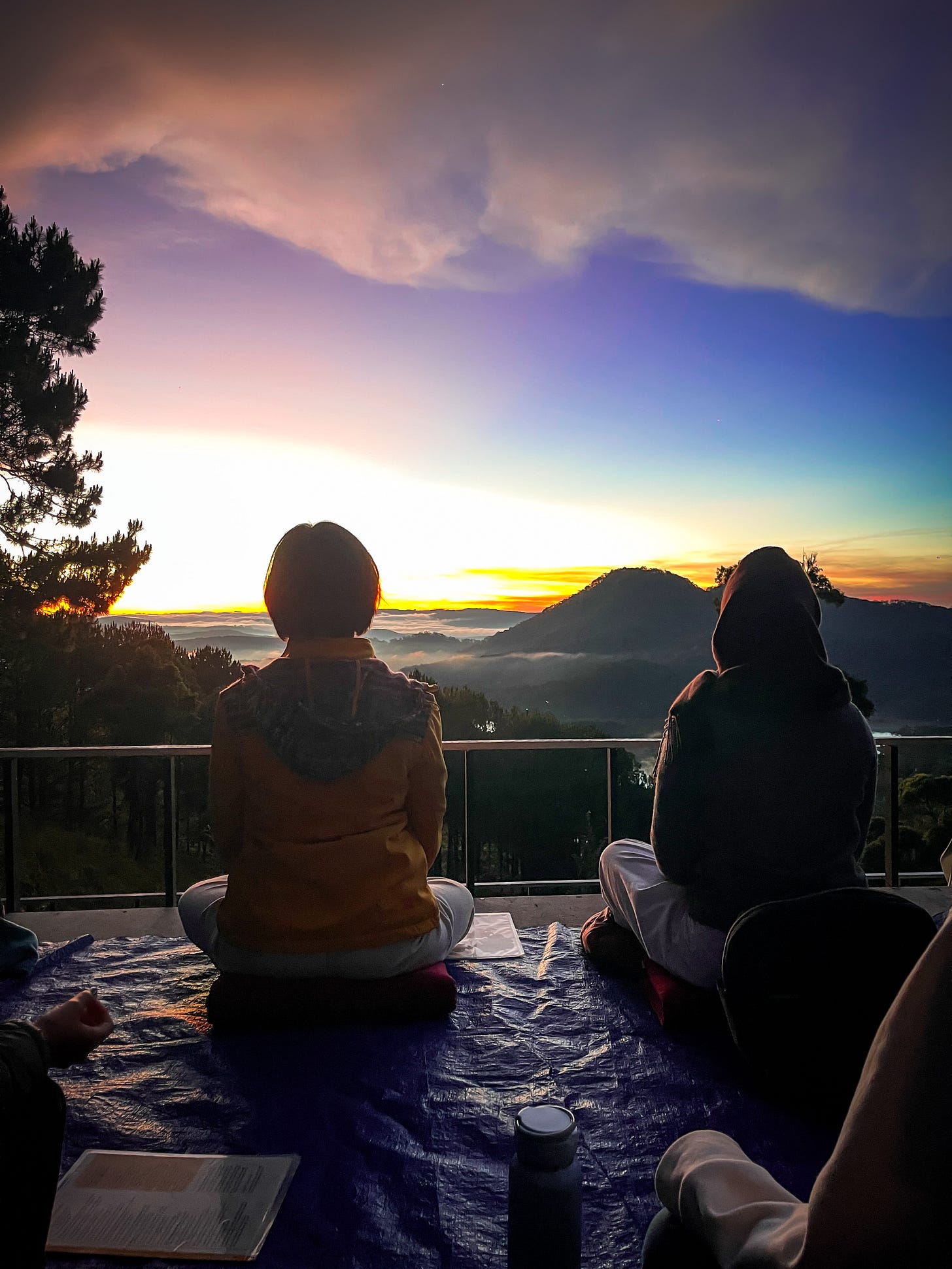 Two women sit cross legged meditating while the sun rises over the clouds in Da Lat, Vietnam
