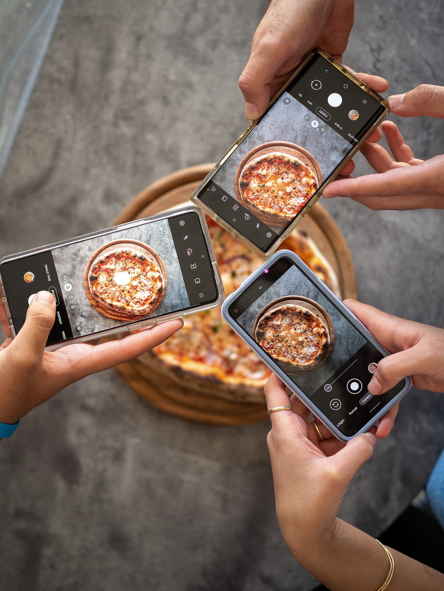 people holding smartphones taking picture of pizza
