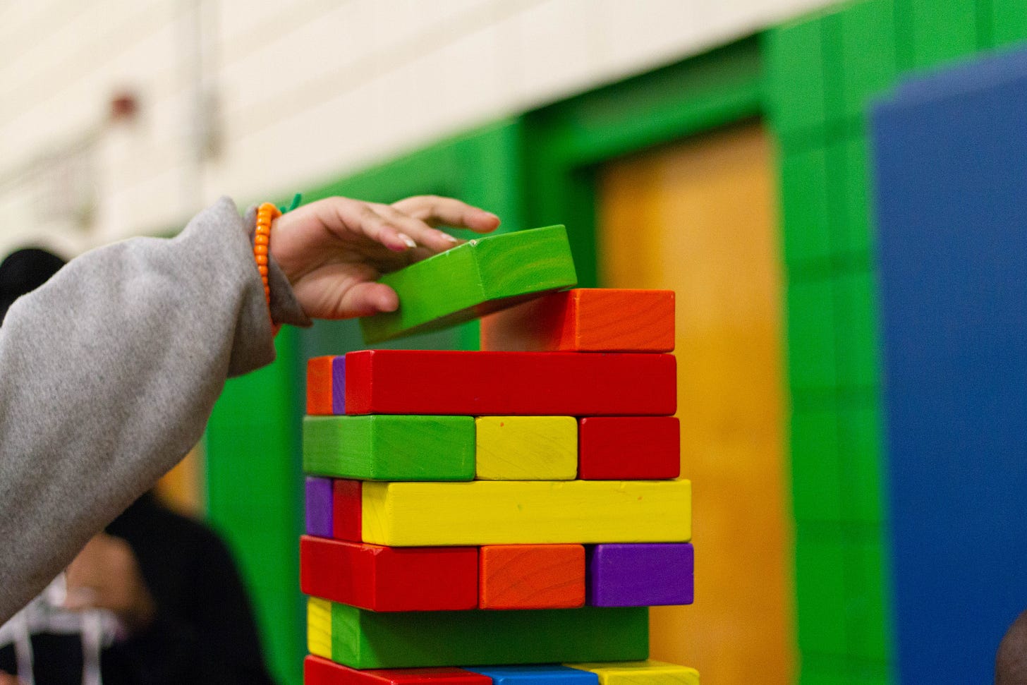A child's hand placing a colorful block on top of a tower of other colorful blocks