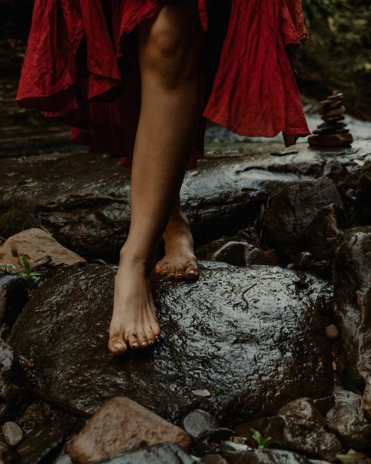 This may contain: a woman in red dress standing on rocks near water with her bare feet propped up This may contain: a woman in red dress standing on rocks near water with her bare feet propped up