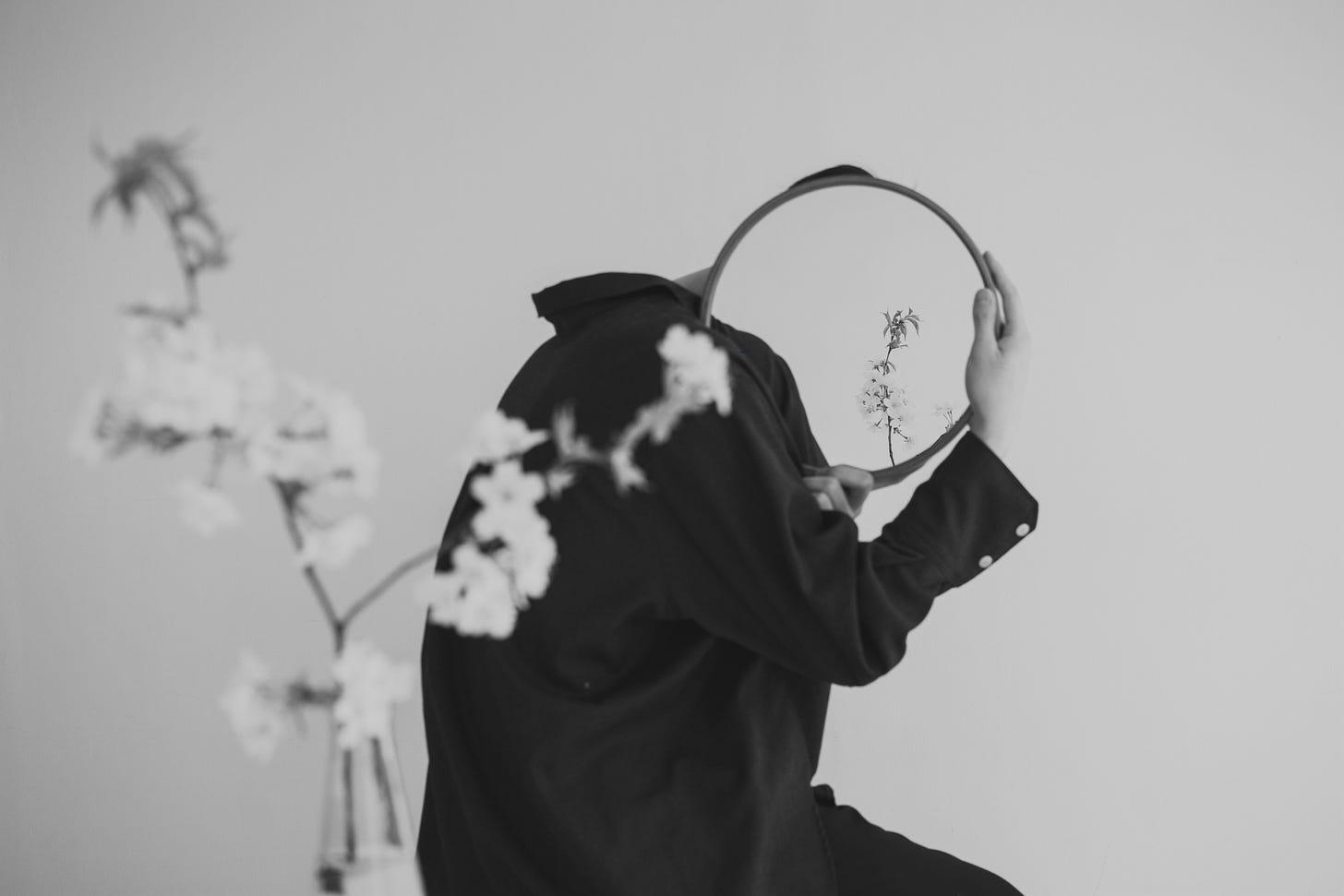 A headless person holds up a mirror, flowers reflect instead of their face, another way for me to hide.