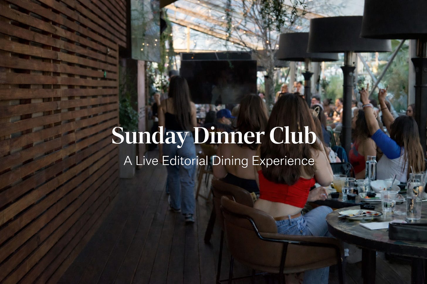 Golden-hour patio dinner scene with guests seated at long tables beneath hanging greenery and outdoor heaters. A woman in a red top sits in the foreground as the centered text reads “Sunday Dinner Club” and “A Live Editorial Dining Experience. Golden-hour patio dinner scene with guests seated at long tables beneath hanging greenery and outdoor heaters. A woman in a red top sits in the foreground as the centered text reads “Sunday Dinner Club” and “A Live Editorial Dining Experience.
