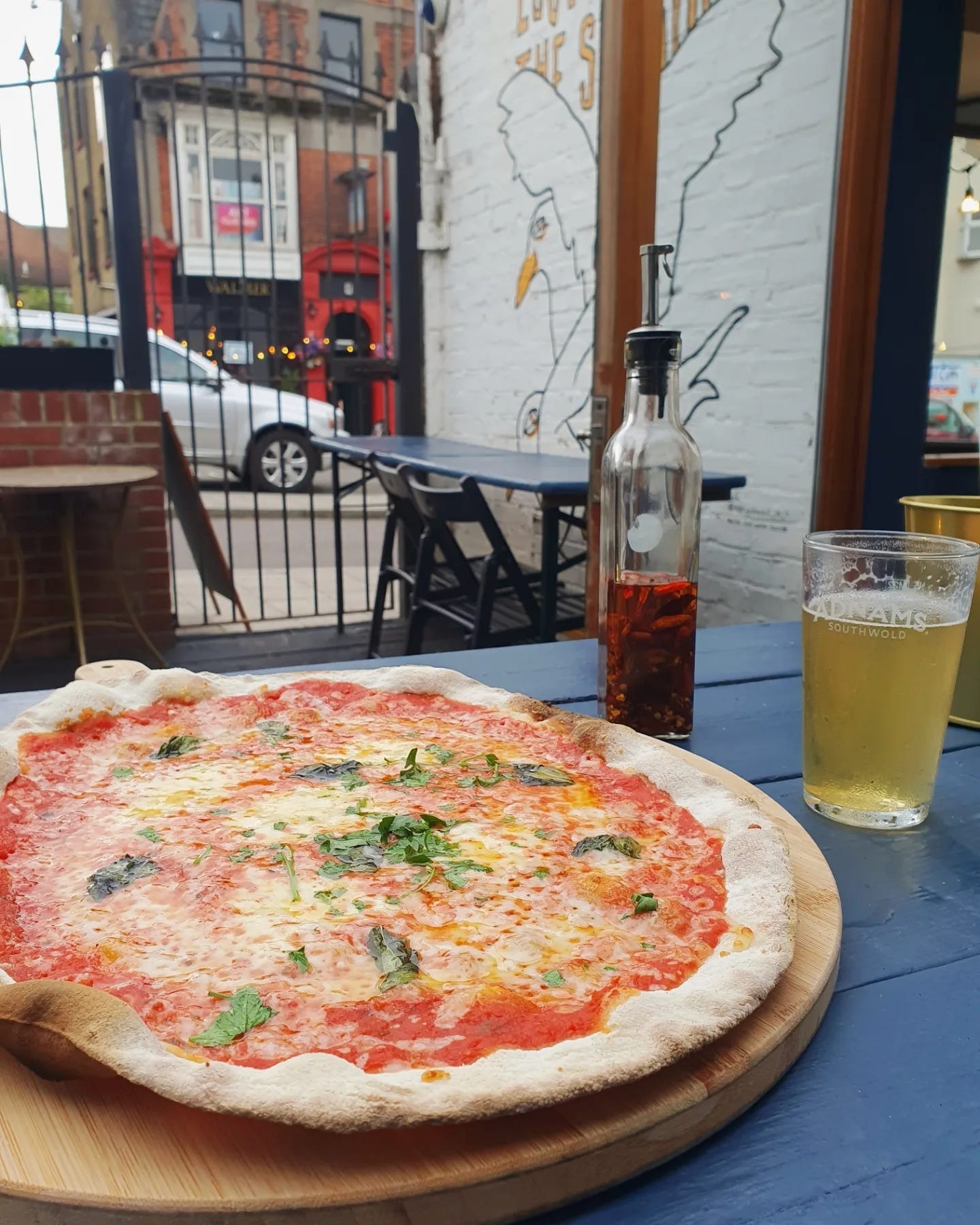 a freshly cooked pizza and a glass of beer on a table outside a pub
