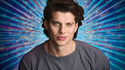 A man in a grey t-shirt smiles, set against a glittering blue background