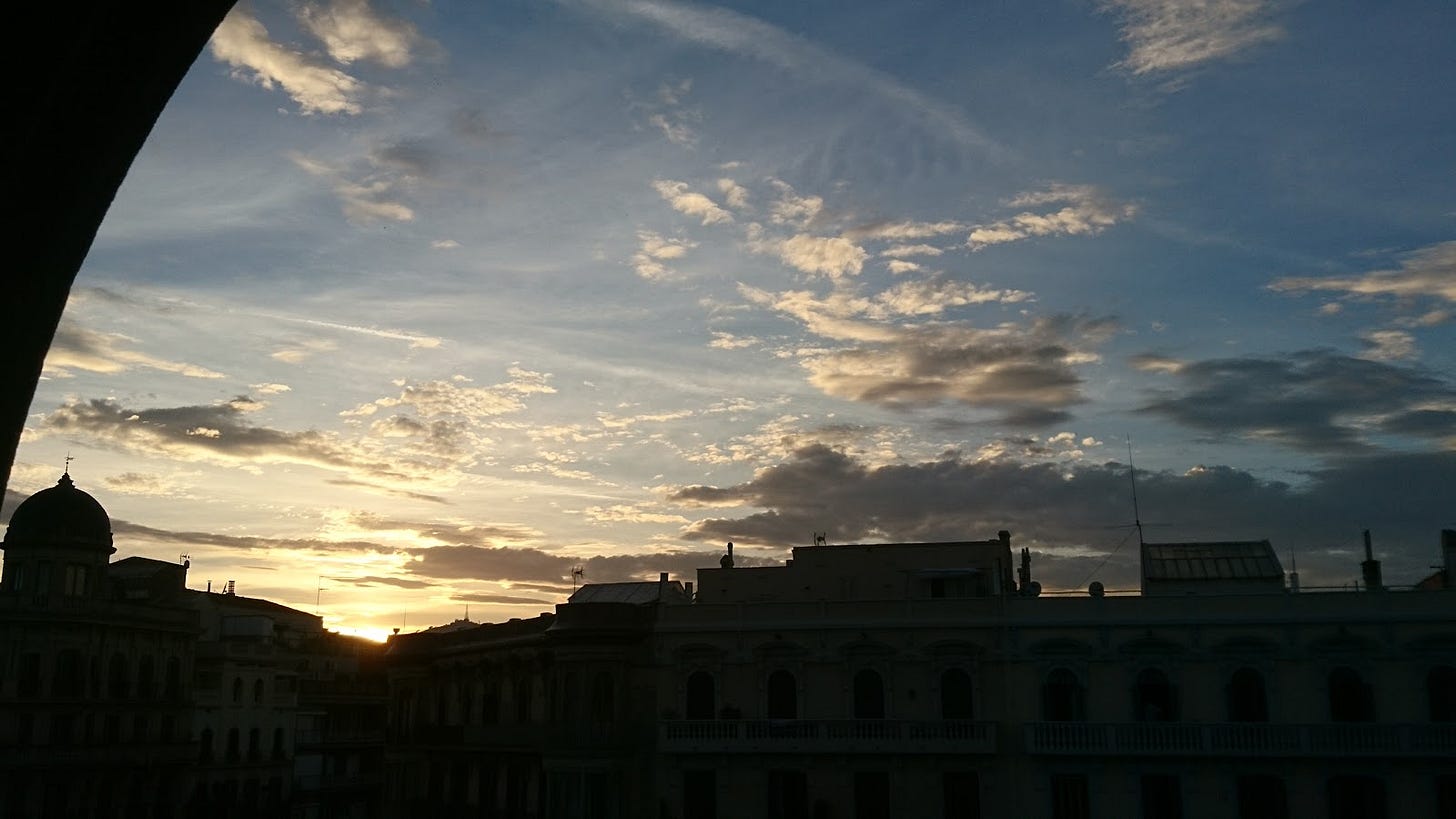 Picture of sunset over a city skyscape with a few clouds on a blue sky