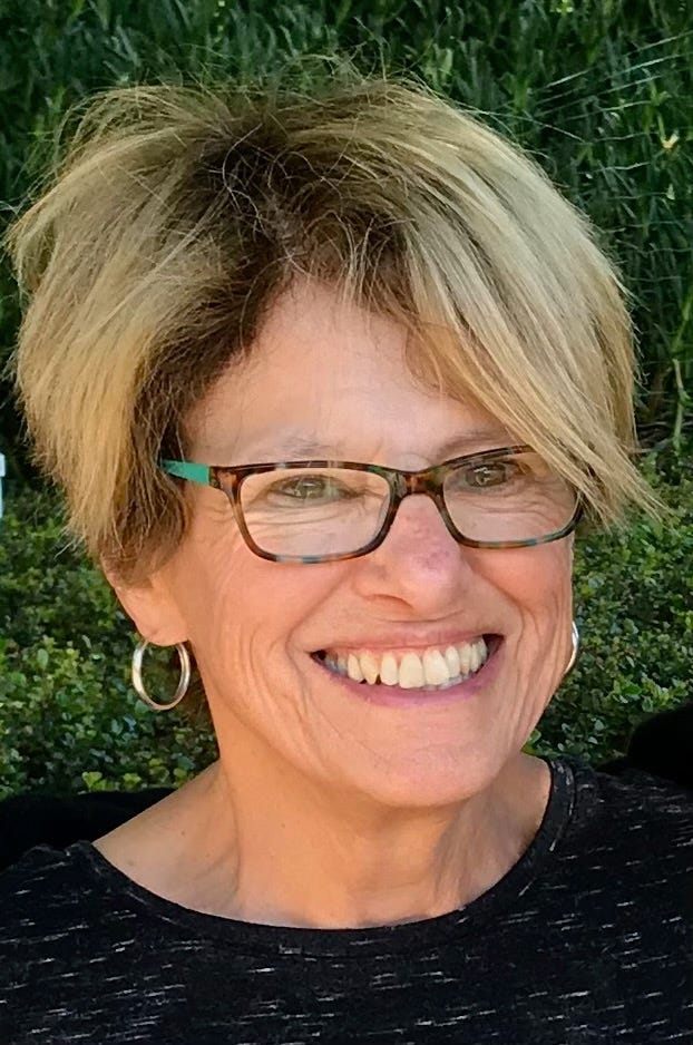 Smiling mid-70's age woman with short stylish hair and glasses with a big smile on her face looking at the camera