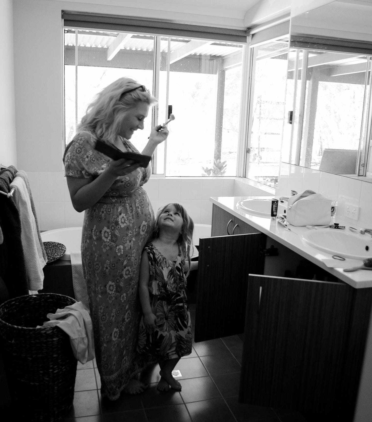 black and white photo of a young girl looking up at her mom as she gets ready in a mirror black and white photo of a young girl looking up at her mom as she gets ready in a mirror