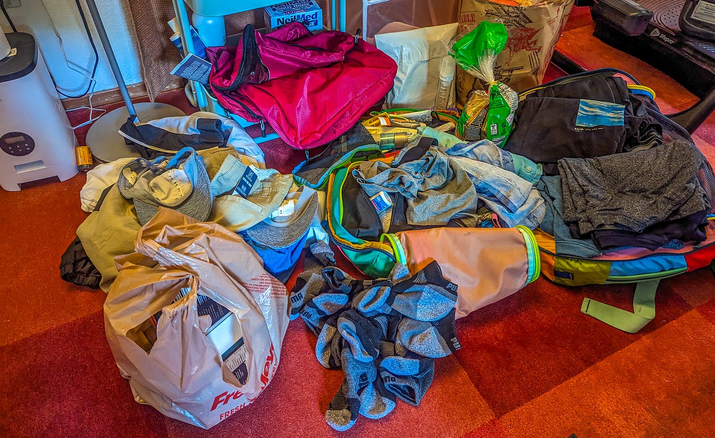 Michael's backpack on the floor, clothes piled up on the floor, a bag of groceries next to it. 