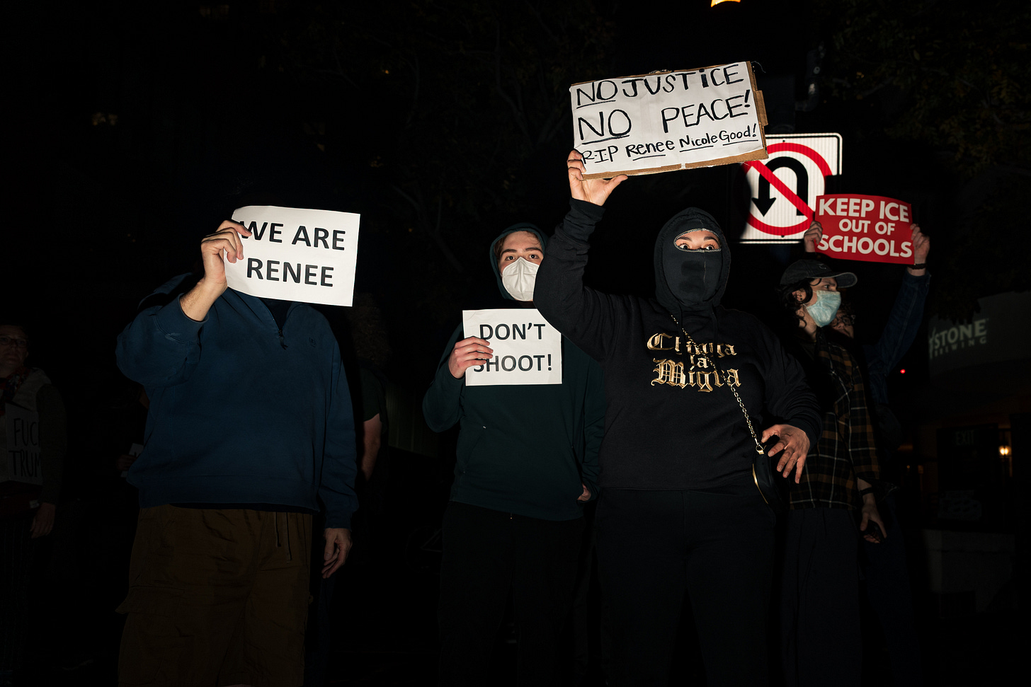 Four people wearing black hold signs supporting Renee Nicole Good and criticizing ICE