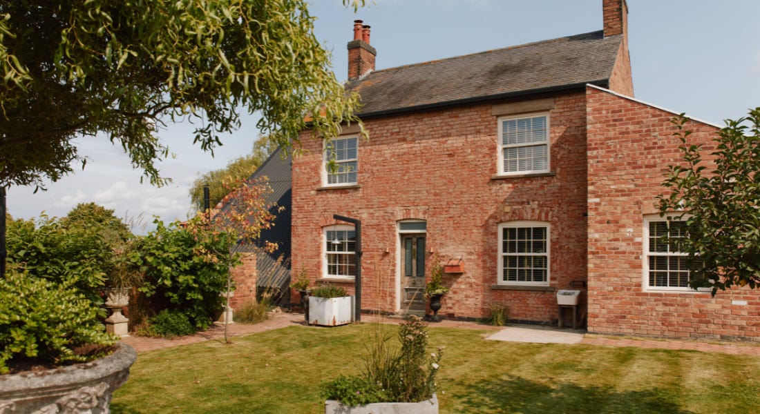 A large brick house with a lawn in front of it and trees hanging next to it