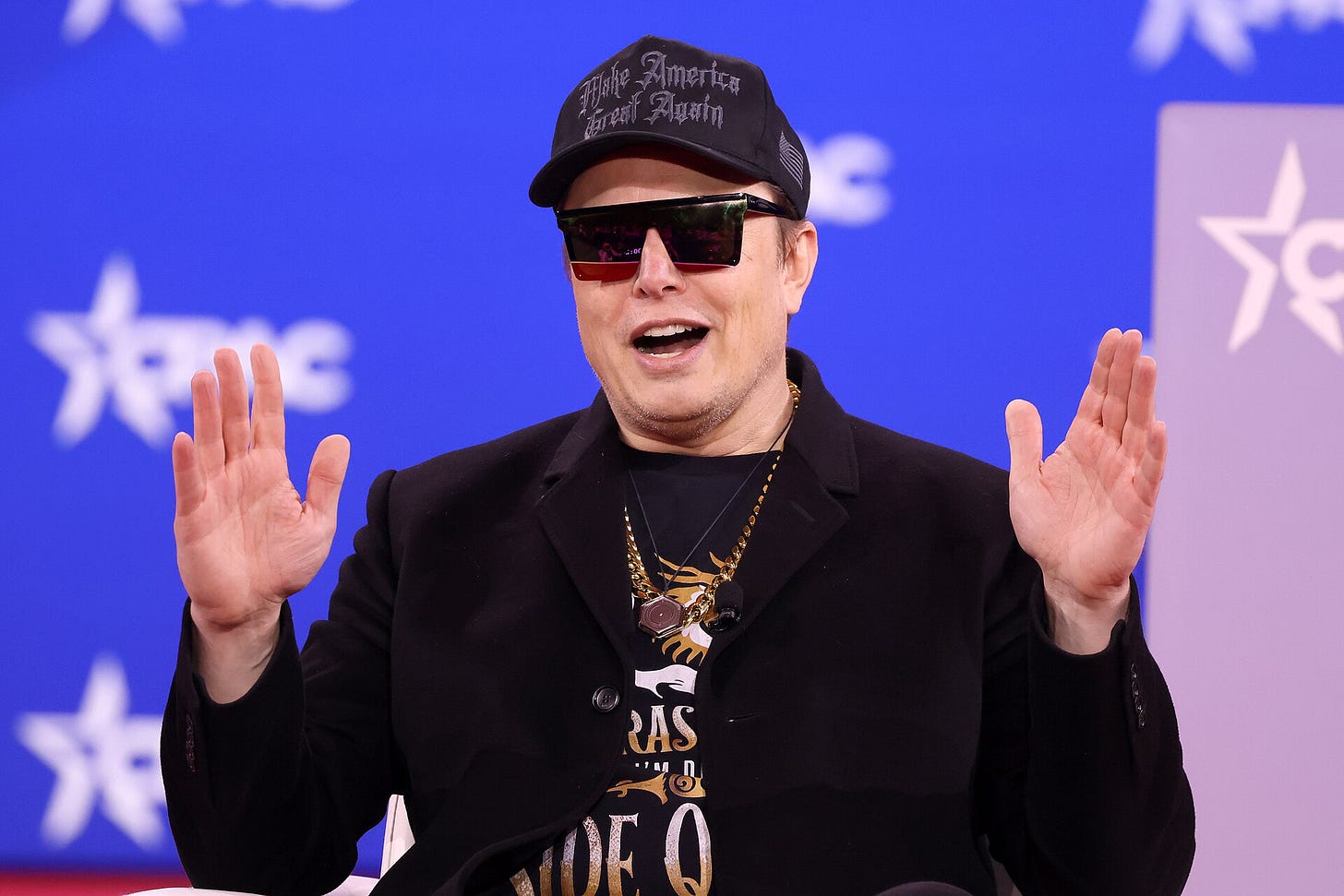 Elon Musk at a podium wearing a Black MAGA hat with fancy script; also wearing sunglasses and a black jacket and gesturing Elon Musk at a podium wearing a Black MAGA hat with fancy script; also wearing sunglasses and a black jacket and gesturing