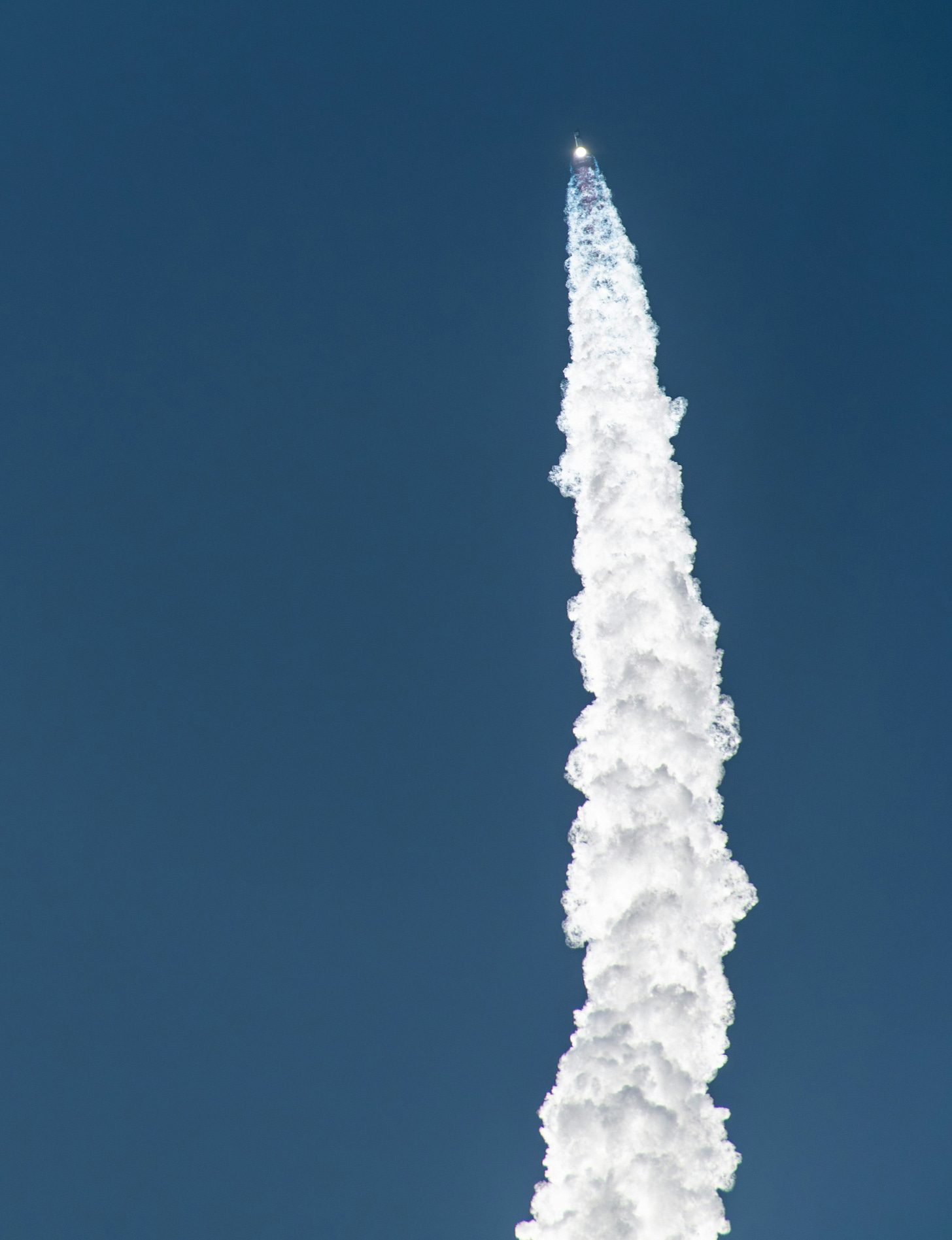 A rocket shoots up into the sky accompanied by a thick cloud of smoke and a curved trail.
