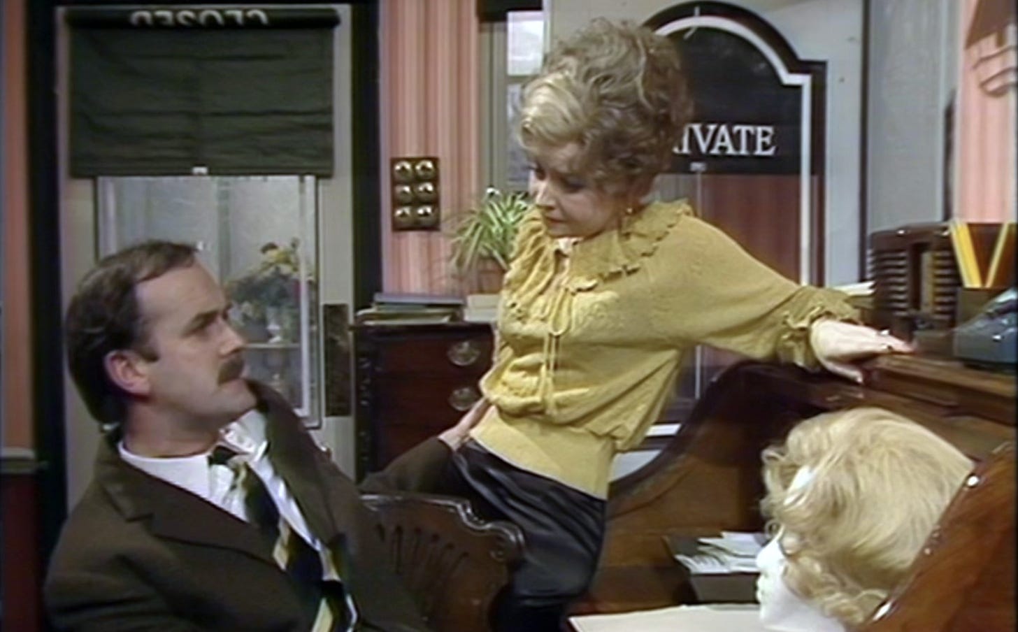 Sybil and Basil Fawlty chatting in their office