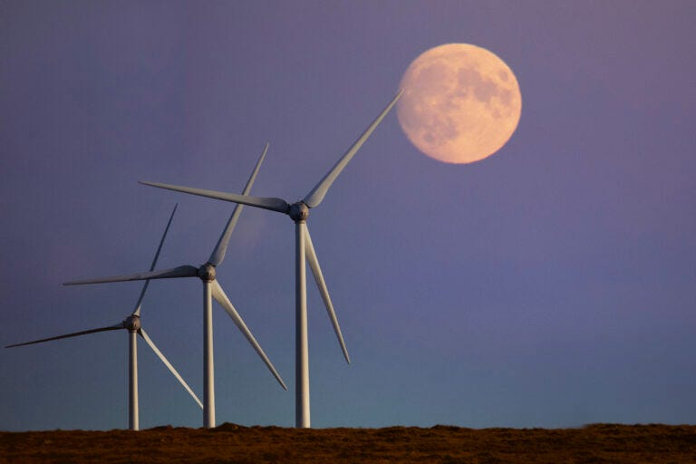 Three windturbines in a row against a purple sky. A dusky full moon is large in the sky. Three windturbines in a row against a purple sky. A dusky full moon is large in the sky.