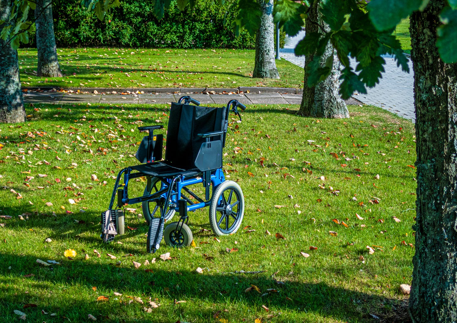 A blue transport chair with its small wheels sitting in a park. 