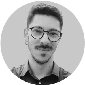 Foto em preto e branco de homem com óculos redondos, barba curta e camisa escura, olhando para a câmera. Foto em preto e branco de homem com óculos redondos, barba curta e camisa escura, olhando para a câmera.