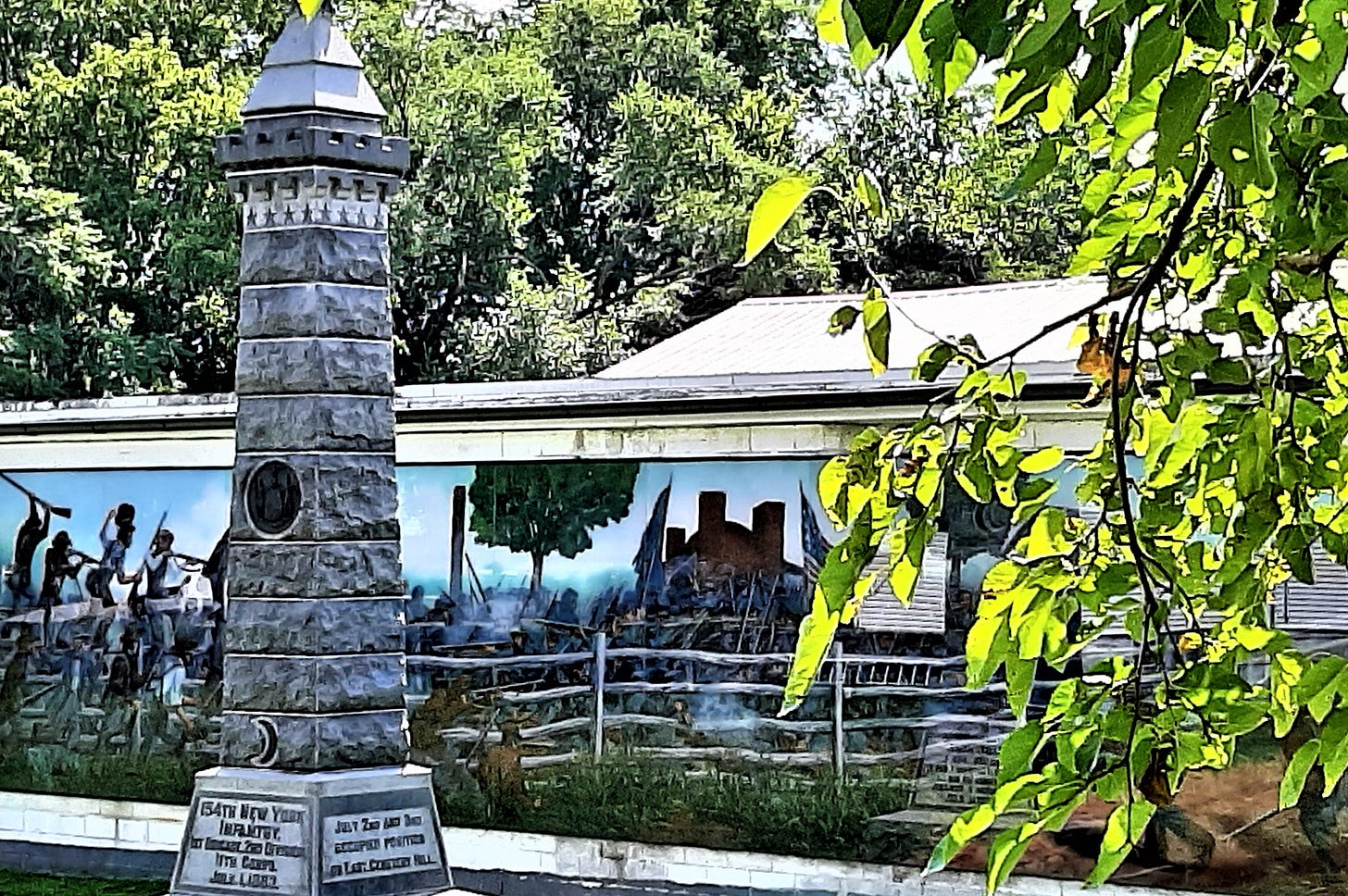 A gray stone monument with a mural on a one-story building in the background.