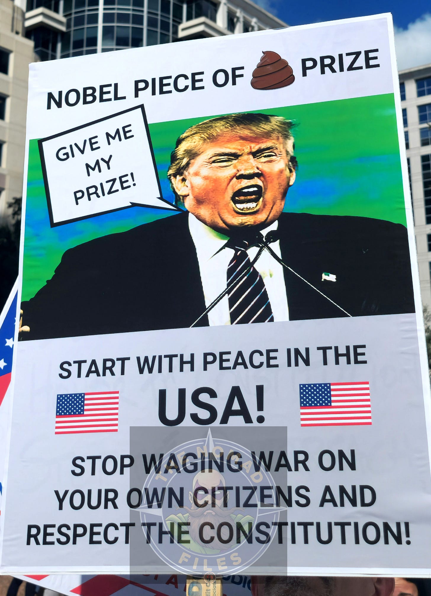 A protest sign titled "NOBEL PIECE OF 💩 PRIZE" featuring a photo of Donald Trump and text urging "START WITH PEACE IN THE USA!"