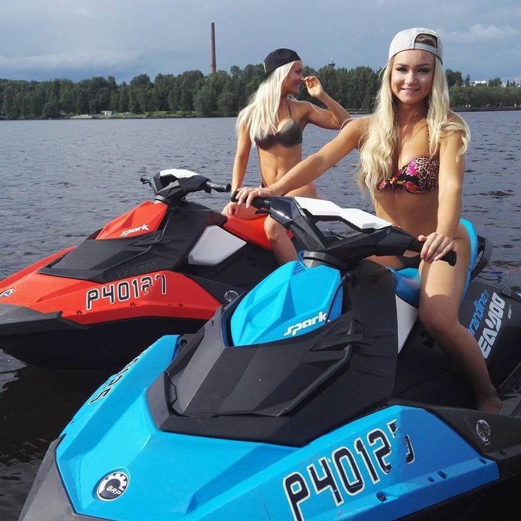 This may contain: two women in bikinis sitting on the back of a blue and black jet ski