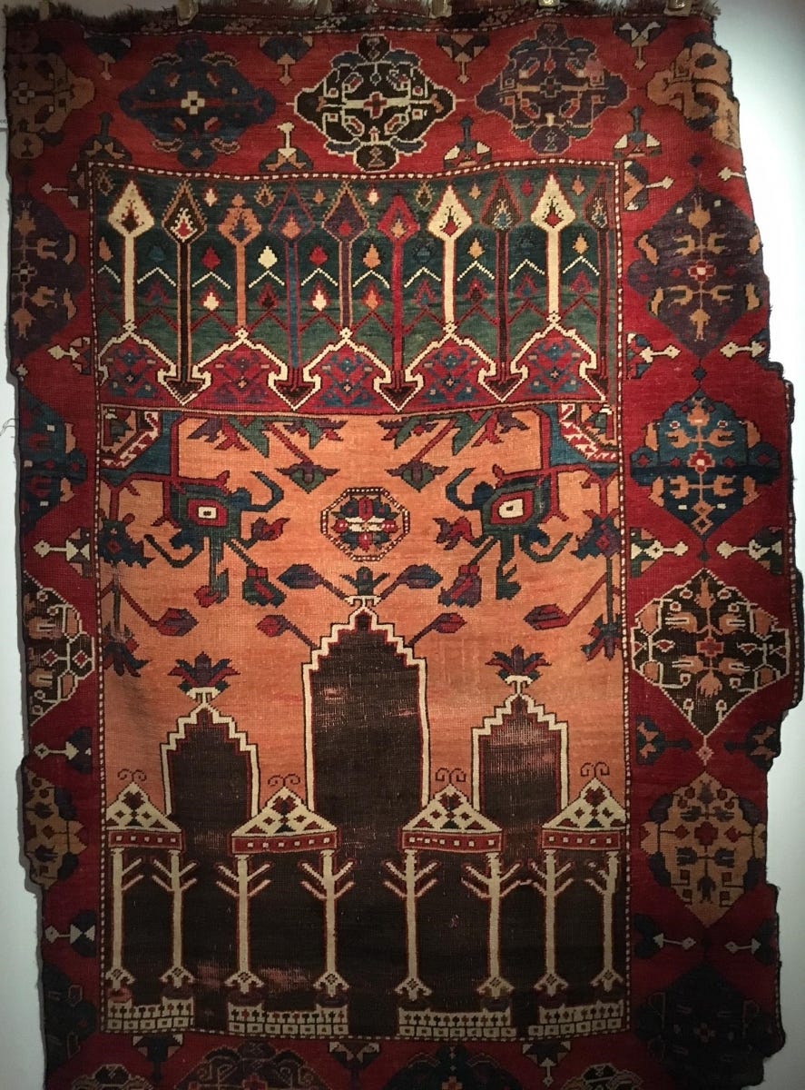 a carpet with a vibrant, warm-colored field at its center, surrounded by a colder, contrasting border. Motifs like trees or rows of spears add texture around the warm field. In the center there are two floral designs that look like glowing eyes. a carpet with a vibrant, warm-colored field at its center, surrounded by a colder, contrasting border. Motifs like trees or rows of spears add texture around the warm field. In the center there are two floral designs that look like glowing eyes.