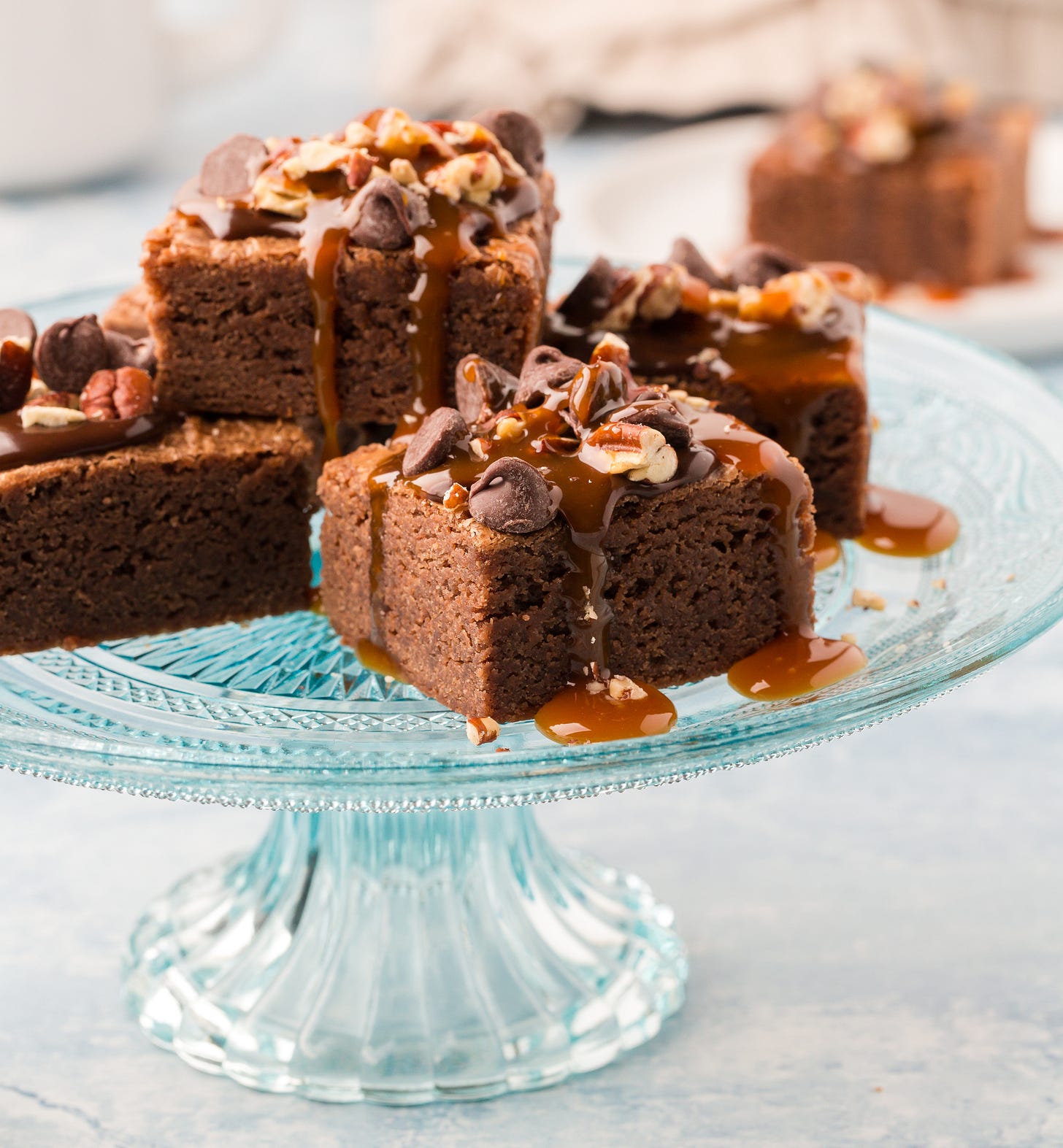 a blue plate of brownies with caramel, chocolate and pecans. 