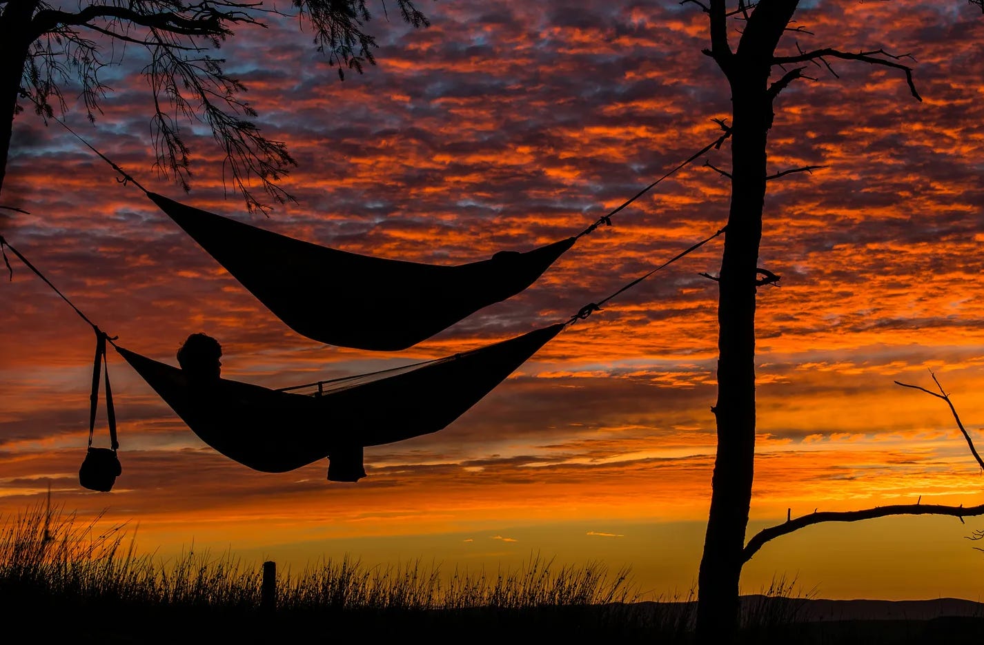 The silhouette of two hammocks set against a red and yellow sunset.