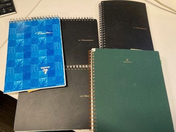 a pile of notebooks and a sheet of graph paper with notes on it in several columns