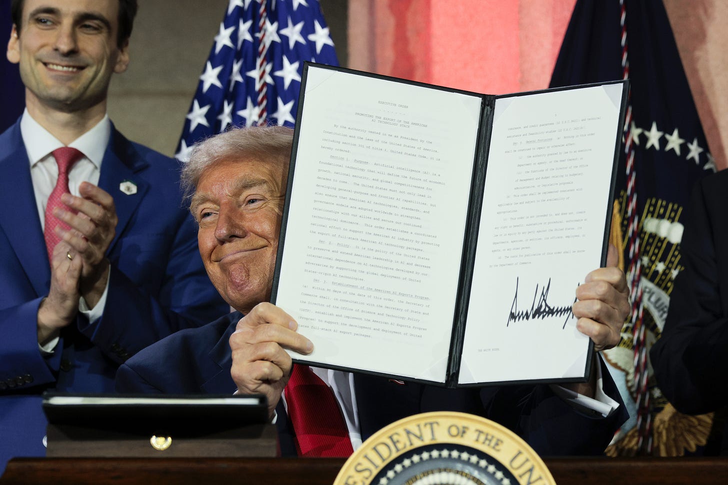 Donald Trump posing and smiling, while holding up a signed executive order.