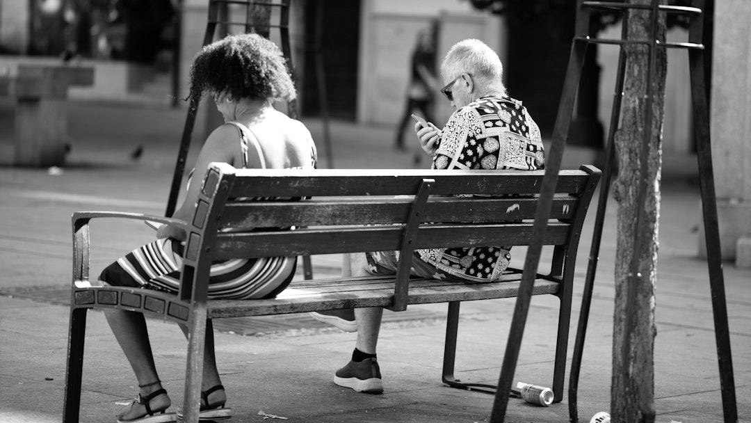 A woman and a man sitting on a wooden bench in a city square A woman and a man sitting on a wooden bench in a city square