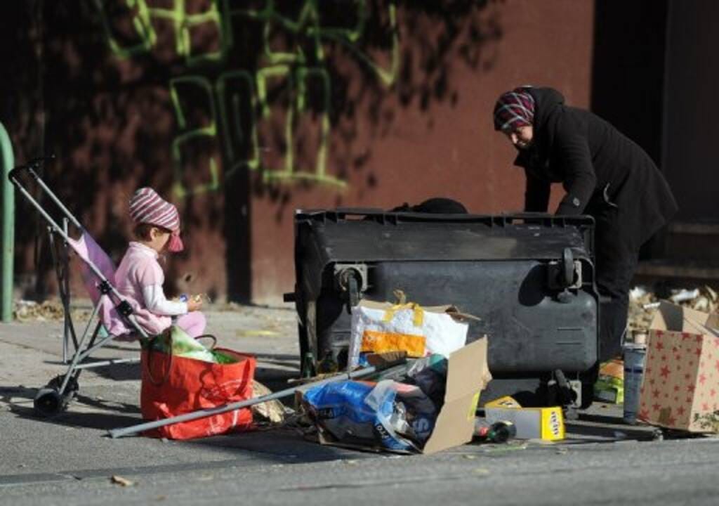 Une femme fouille dans les poubelles devant son enfant en poussette