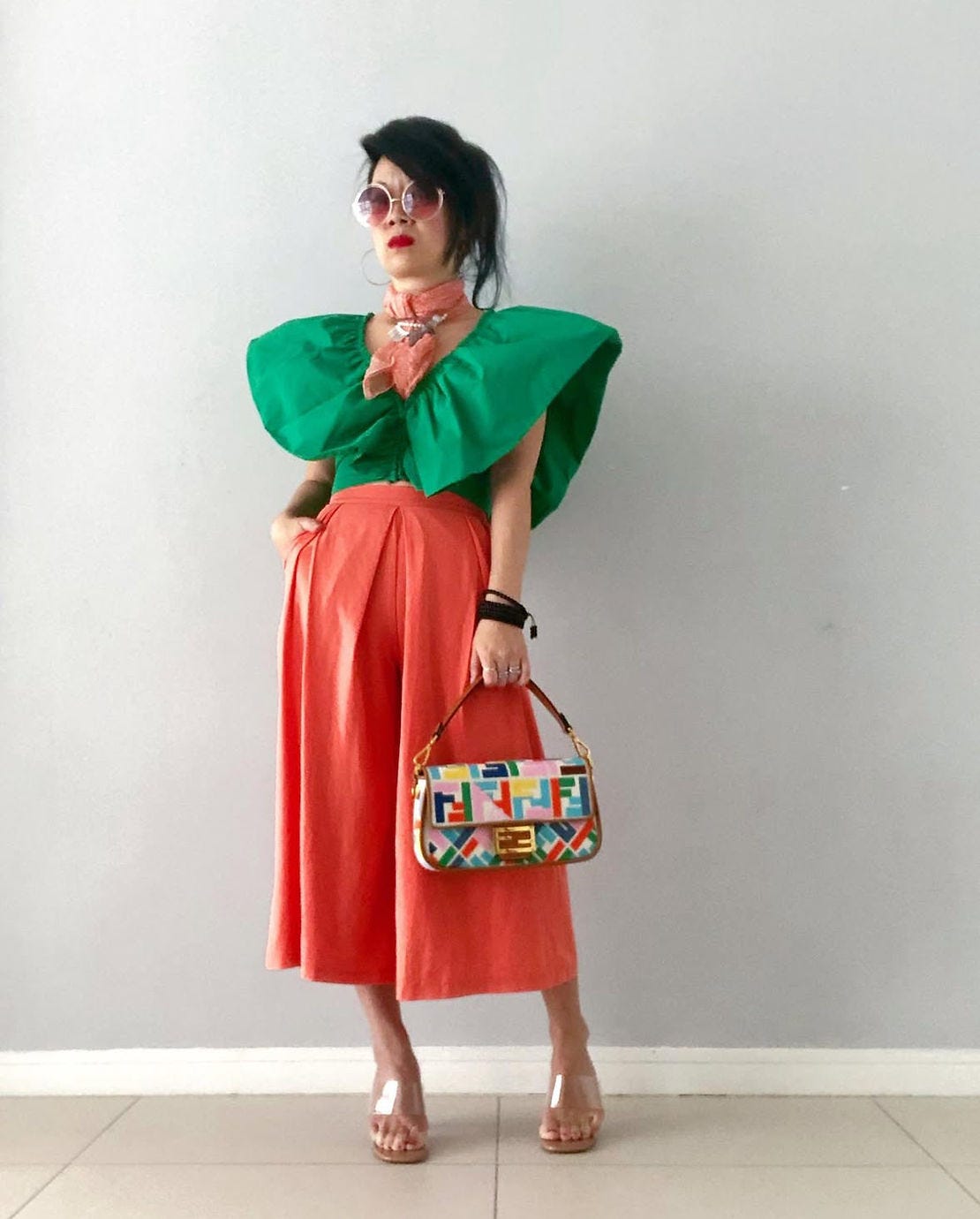 Cancer survivor Sarah poses in green top and orange skirt, holding colorful bag. Cancer survivor Sarah poses in green top and orange skirt, holding colorful bag.