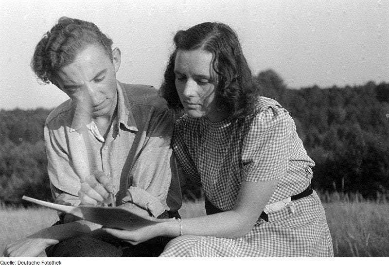 A historical photo of a young man and woman reading together outdoors.