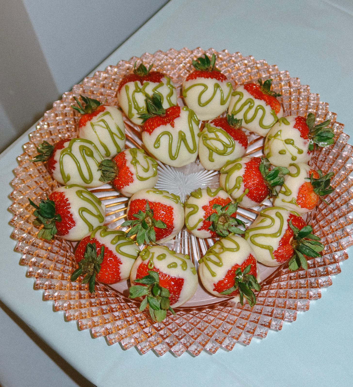 Platter of white-chocolate strawberries drizzled with green icing arranged in a circle.