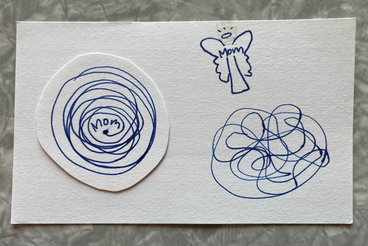 Blue ink sketches on a white index card. On the left side is the word Mom above a dot from which a line spirals outward ... and in ... and out ... forming irregular concentric circles. On the right side is the word Mom up higher, below a halo, and between two angel/butterfly wings. Below the Angel Mom is a squiggly line, loosely traveling around the shape of a circle but more random than that. 