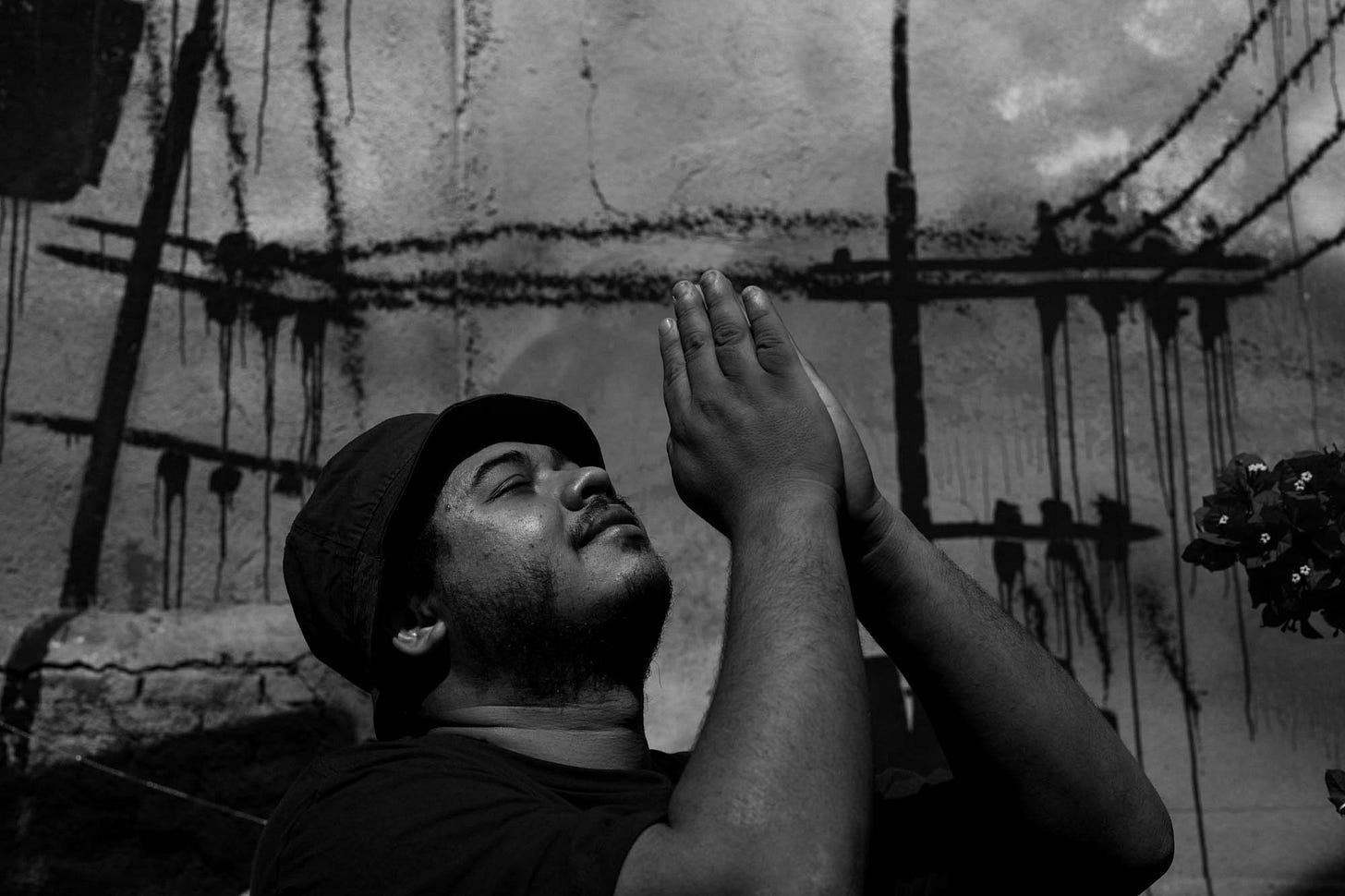 Fotografia em preto e branco mostra Thiago Vinicius com as mãos levantadas para o céu, em prece. Fotografia em preto e branco mostra Thiago Vinicius com as mãos levantadas para o céu, em prece.
