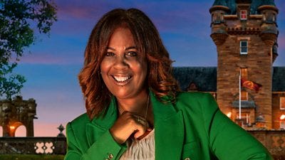 A woman in a light top and green jacket smiles to camera, set against the backdrop of a castle by night A woman in a light top and green jacket smiles to camera, set against the backdrop of a castle by night
