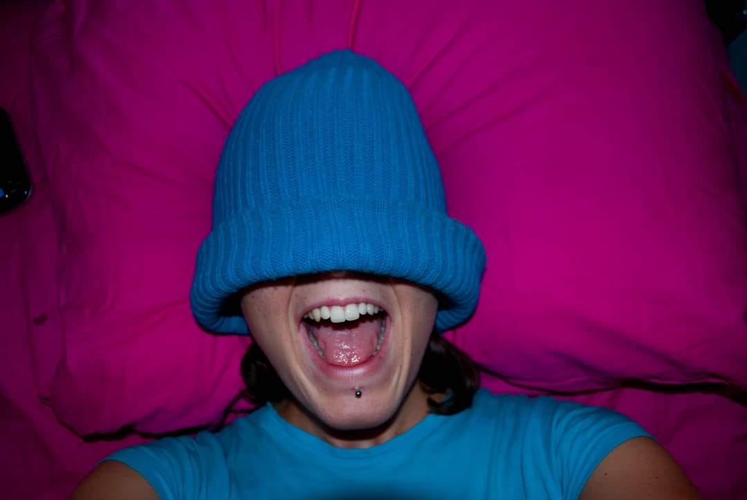 The picture shows a white woman who looks like she is screaming with half her face covered by a blue hat.