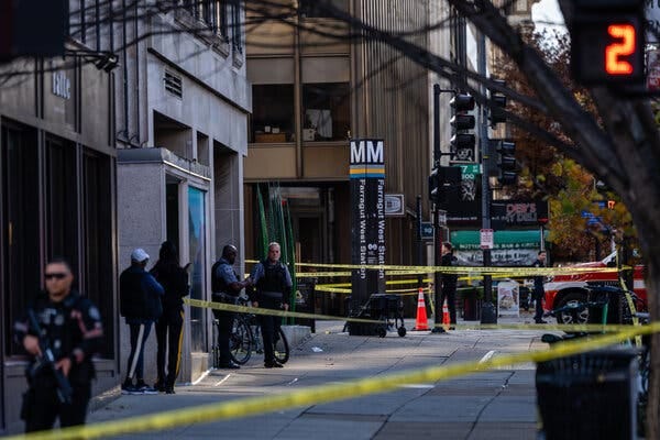 Crime scene tape stretches across a street. Law enforcement officers stand nearby.